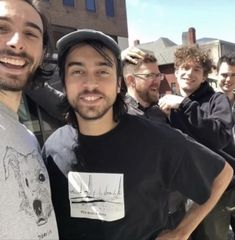 a group of men standing next to each other in front of a brick building on a sunny day