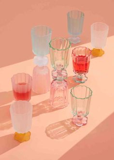 several different colored glass vases sitting on a white table with pink and yellow shadows