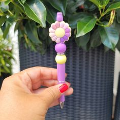 a person holding a purple and yellow flower shaped pen in front of a potted plant