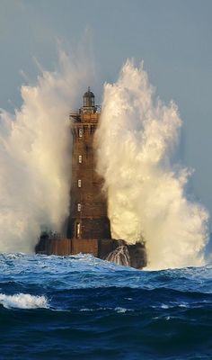 a large wave crashes over a lighthouse in the middle of the ocean as it breaks into the water