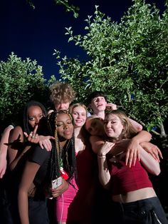 a group of young people standing next to each other in front of trees and bushes