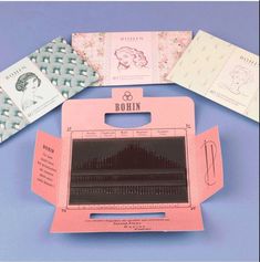 an open pink box with several different types of sewing needles in it on a blue surface