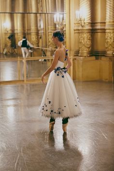 a woman in a white and blue dress is looking at something on the ground while another person stands behind her