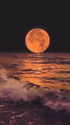 a full moon over the ocean with waves coming in to shore and an orange hued sky