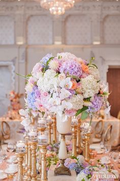 a table topped with lots of gold vases filled with purple and white flowers next to candles