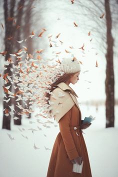 a woman is standing in the snow with birds flying around her head and holding a book