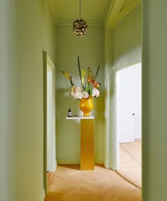 a yellow vase with flowers in it sitting on top of a wooden table next to an open door