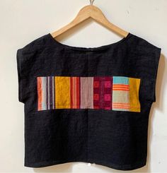 a black top with multicolored stripes on the front and back, hanging from a wooden hanger