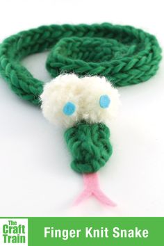 a green and white knitted snake with blue eyes on it's head, sitting on a white surface