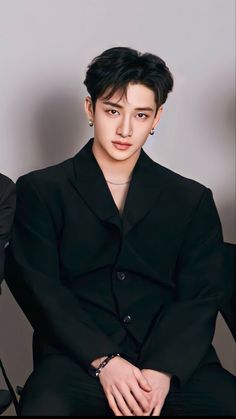 the young man is sitting down wearing a black suit