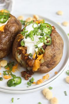 two loaded baked potatoes on a plate with green onions and sour cream cheese toppings