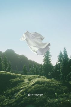 a white cloth flying in the air over a lush green hillside covered in trees and grass