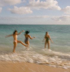 three girls are playing in the water at the beach while one girl is jumping into the ocean