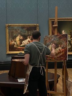 a man standing in front of two paintings on easels and holding a paintbrush