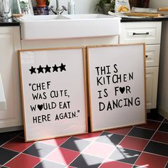 two framed posters sitting on the floor in a kitchen next to a sink and counter