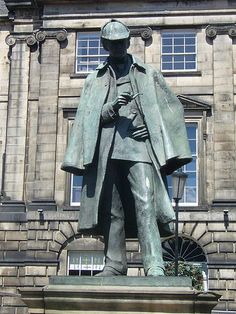 a statue of a man wearing a coat and hat in front of a stone building