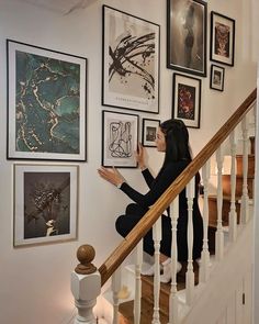 a woman is sitting on the stairs and looking up at pictures hanging on the wall