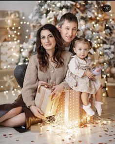 a man and woman are holding a baby in front of a christmas tree with presents