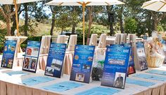 several tables with umbrellas and signs on them at an outdoor event in the sun