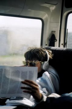 a man wearing headphones and reading a newspaper on a train with the window open