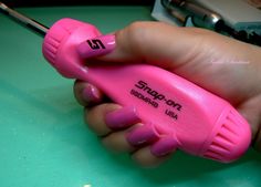 a hand holding a pink nail polisher on top of a table