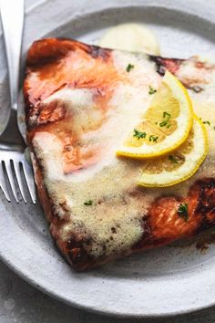 a white plate topped with meat covered in sauce and lemon slices next to a fork