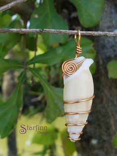 a white and gold wire wrapped pendant hanging from a tree branch