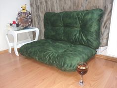 a green futon couch with a glass of wine on the floor next to it