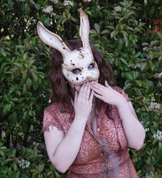 a woman wearing a bunny mask standing in front of bushes with her hands on her face