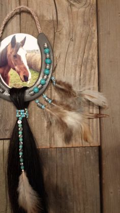 a native american dream catcher with a horse on it's head and feathers hanging from the side