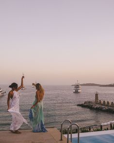 two women standing on the edge of a swimming pool, one holding a wine glass in her hand