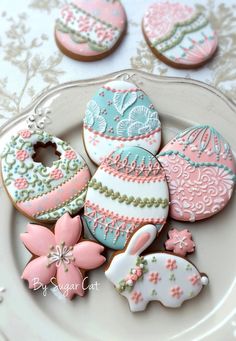 some decorated cookies are on a plate with pink and blue frosted eggs in the background