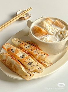 a white plate topped with dumplings next to a bowl of soup and chopsticks