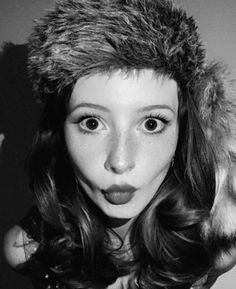 a black and white photo of a woman with long hair wearing a fur hat on top of her head