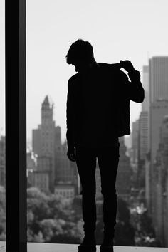 a man standing in front of a window looking out at the city