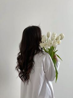 a woman holding a bouquet of white tulips in front of her face and back to the camera