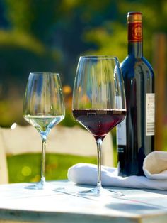 two wine glasses sitting on top of a table next to bottles of wine and napkins