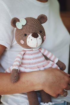 a crocheted teddy bear is held by a person's arm, wearing a pink and white striped dress