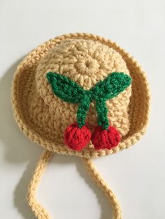 a crocheted hat with two cherries on the front and green leaves on the back