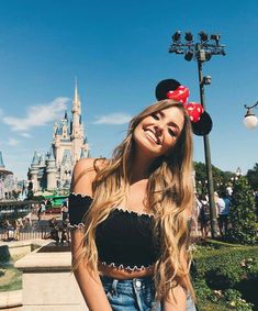 a woman standing in front of a castle with a red minnie mouse head on her head