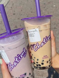 two people holding up drinks with purple straws on the top and one is filled with milkshakes