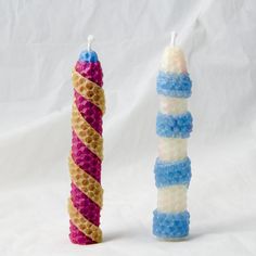 two colorful candles are next to each other on a white background, one is made out of honeycombs