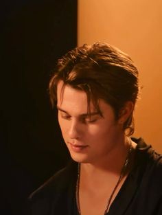 the young man is looking down at his cell phone while wearing a black shirt and necklace