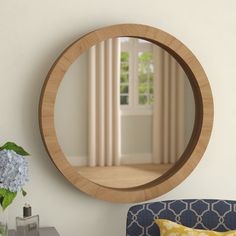 a round mirror on the wall above a blue chair and vase with hydrangeas