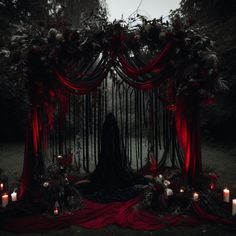 a person standing in front of a red and black altar with candles on the ground