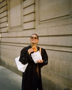 a woman is standing on the sidewalk and eating some food while holding her hand in her pocket