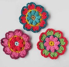 three crocheted flower appliques on a white surface, each with different colors