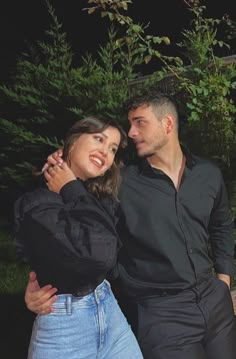 a man and woman are posing for a photo in front of some trees with their arms around each other