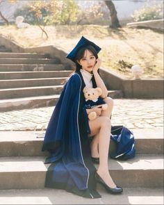 a woman sitting on steps with a teddy bear wearing a graduation gown and holding a teddy bear