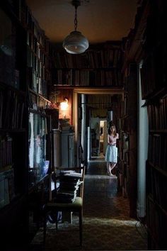 a woman standing in a dark room next to bookshelves